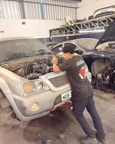 Mecânico da LF, com o uniforme da oficina, trabalhando no motor de uma picape de capô aberto