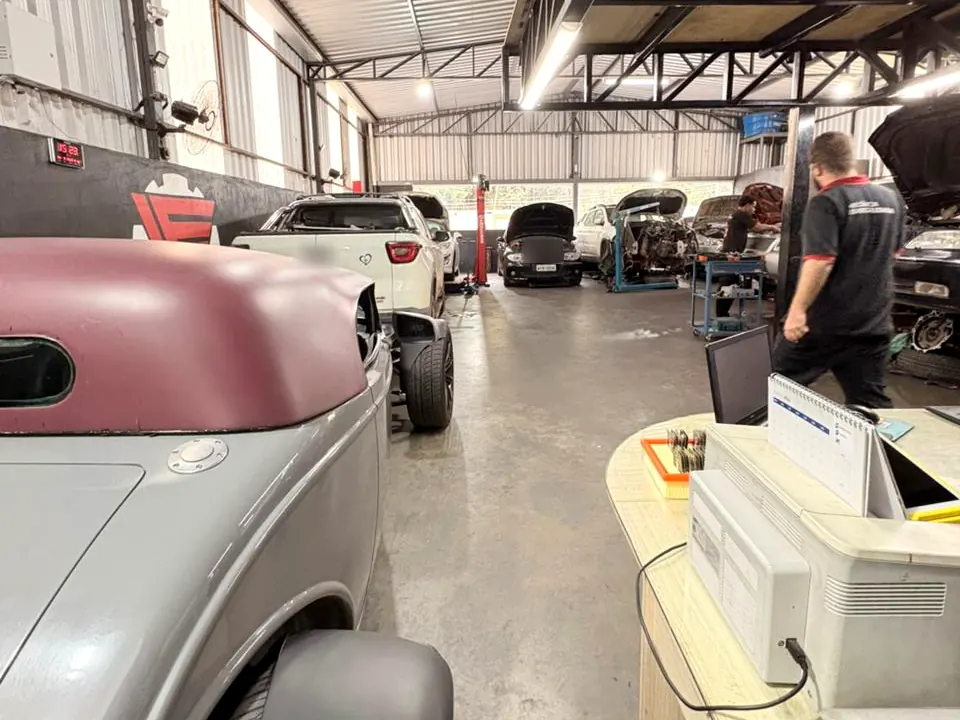 Oficina da LF por dentro, com carros em manutenção e mecânico de uniforme