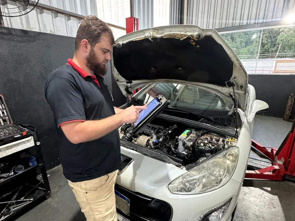 Mecânico da LF lendo a central de um carro com scanner de diagnóstico, de capô aberto